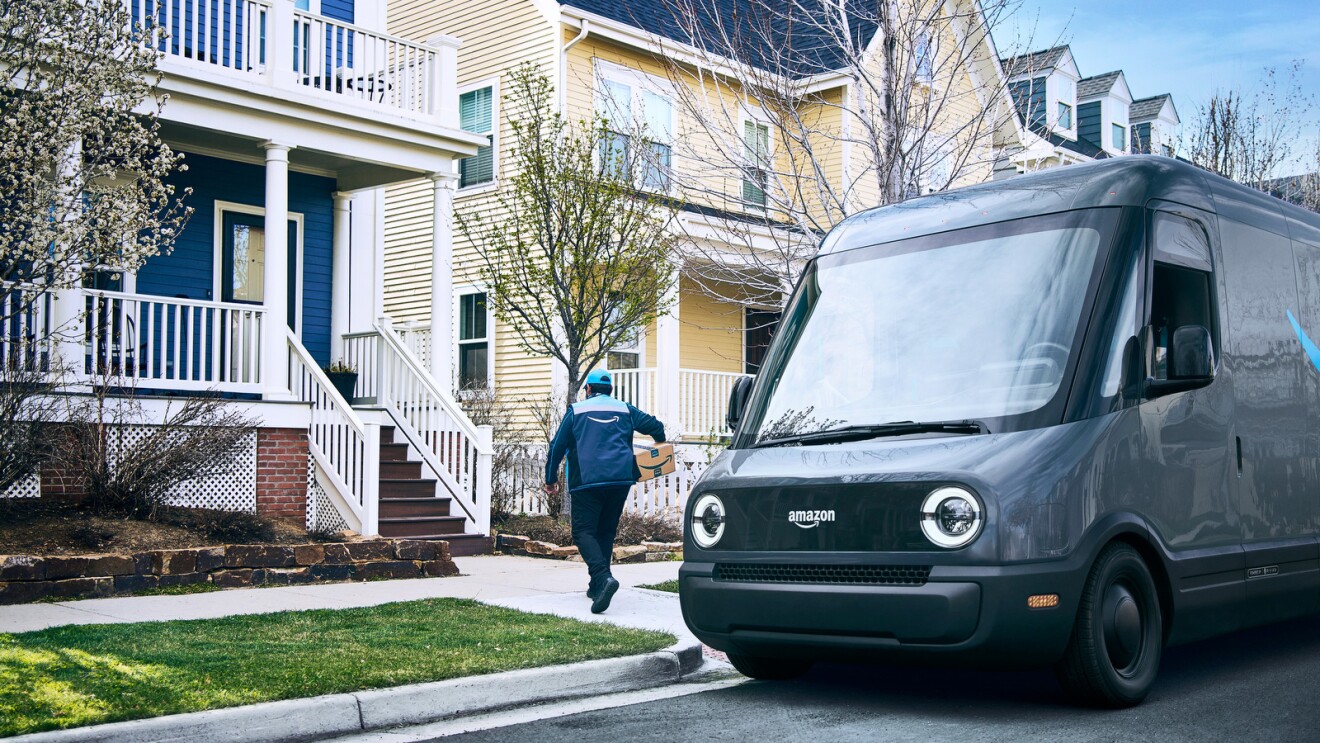 An Amazon driver walks a package from a Rivian delivery van to a customer's home.